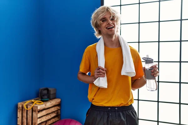 Young blond man smiling confident drinking water at sport center