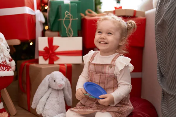 愛らしいです白人女の子遊びますプレートとフォークおもちゃで床に座っていますクリスマスツリーによってホーム — ストック写真