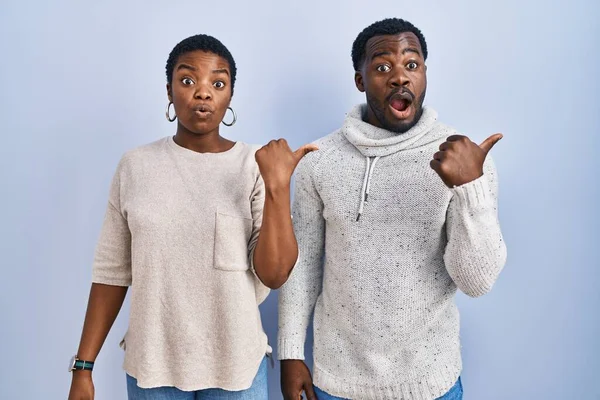 年轻的非洲裔美国夫妇站在蓝色的背景上 手指头指向侧面 张开嘴惊讶地看着 — 图库照片