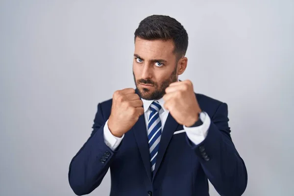 Handsome hispanic man wearing suit and tie ready to fight with fist defense gesture, angry and upset face, afraid of problem