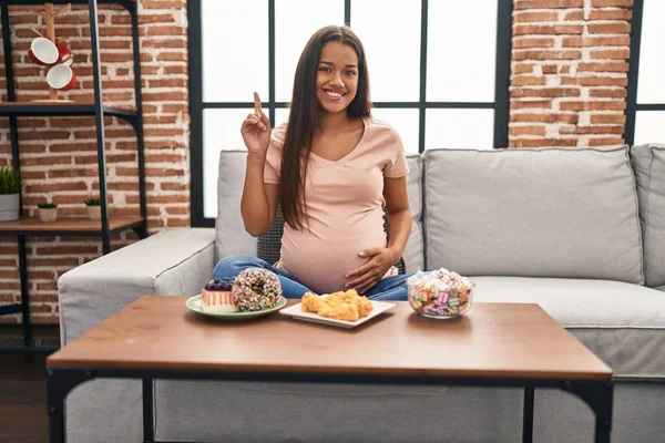 若いです妊娠中の女性食べるお菓子で自宅驚きでアイデアや質問を指差す指で幸せな顔 ナンバーワン — ストック写真