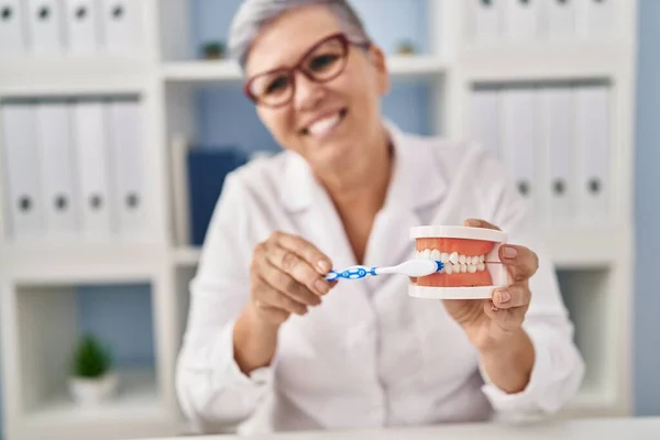 Middle age woman wearing dentist uniform teaching to wash tooth at clinic