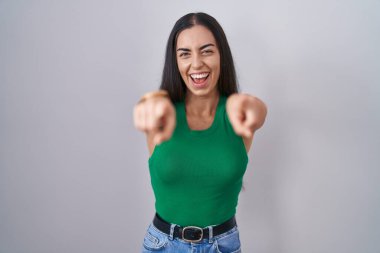 Young woman standing over isolated background pointing to you and the camera with fingers, smiling positive and cheerful 