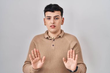 Non binary person standing over isolated background moving away hands palms showing refusal and denial with afraid and disgusting expression. stop and forbidden. 