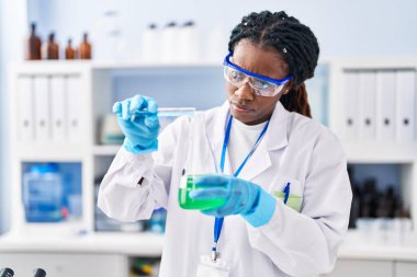 Laboratuvarda test tüpüne sıvı döken Afrikalı Amerikalı kadın bilim adamı.