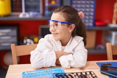 Sevimli İspanyol kız öğrenci gülümsüyor. Kollarını kavuşturup sınıfta oturuyor.