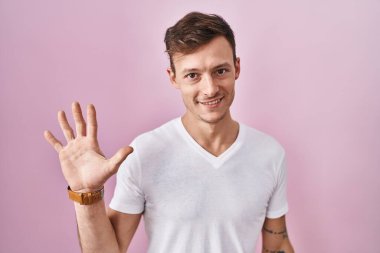 Caucasian man standing over pink background showing and pointing up with fingers number five while smiling confident and happy. 
