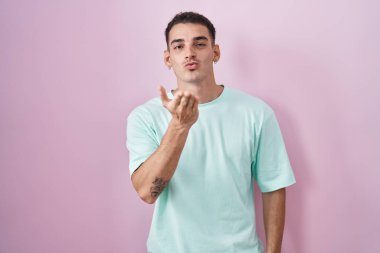 Yakışıklı İspanyol bir adam pembe arka planda dikiliyor kameraya bakıyor ve havada bir öpücük savuruyor. Güzel ve seksi. aşk ifadesi. 