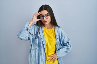 Young hispanic woman standing over blue background worried and stressed about a problem with hand on forehead, nervous and anxious for crisis 