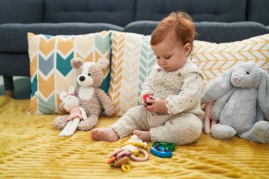 Sevimli kızıl saçlı bebek evdeki kanepede oturmuş oyuncak arabasıyla oynuyor.