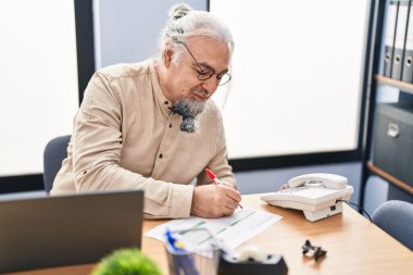 Middle age grey-haired man business worker using laptop writing on document at office