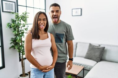 Bir bebek bekleyen, hamile karnına dokunan, dillerini mutlu bir ifadeyle dışarı çıkaran ırklar arası genç bir çift. duygu kavramı. 