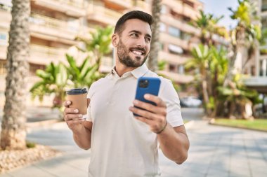 Genç İspanyol adam akıllı telefon kullanıyor, sokakta kahve içiyor.