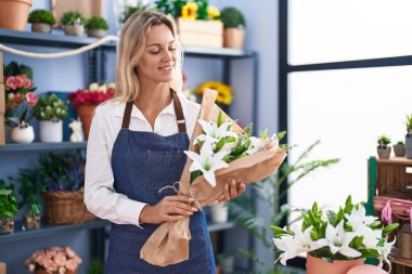 Young blonde woman florist holding bouquet of flowers at florist
