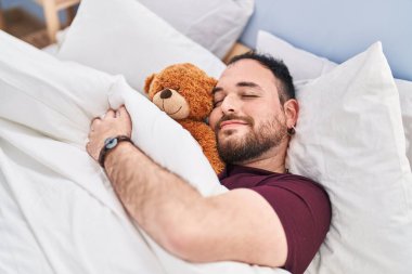 Genç İspanyol adam, oyuncak ayıyı kucaklıyor. Yatakta yatıyor, yatak odasında uyuyor.