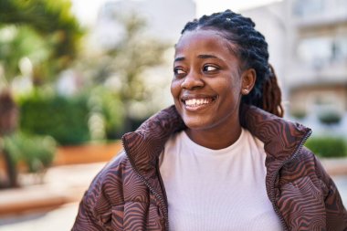 Afro-Amerikalı kadın gülümsüyor, parkın kenarına bakıyor.