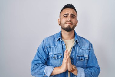 Tecrit edilmiş arka planda duran genç İspanyol adam elleri bağlı yalvarıyor ve dua ediyor. Yüzünde umut ifadesi var. Çok duygusal ve endişeli. Yalvarıyor. 