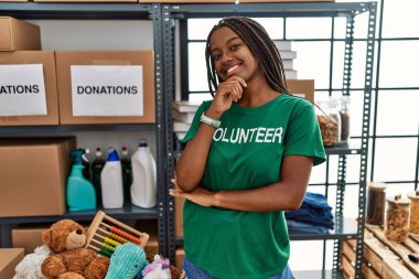 Bağışlarda gönüllü tişört giyen Afro-Amerikalı genç bir kadın kameraya kollarını kavuşturup gülümseyen ve çenesini kaldırmış bir şekilde bakıyor. Olumlu düşünmek. 