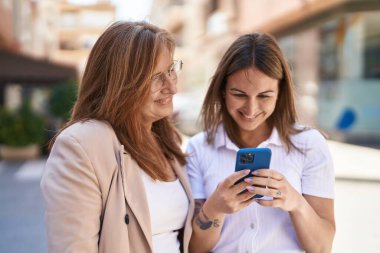 Mother and daughter using smartphone standing together at street