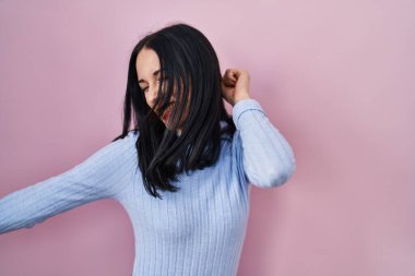 Hispanic woman standing over pink background dancing happy and cheerful, smiling moving casual and confident listening to music 