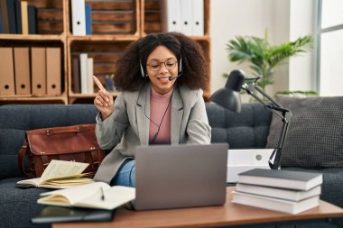 Young african american woman doing online session at consultation office smiling happy pointing with hand and finger to the side 