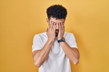 Arap adam sarı arka planda duruyor. Yorgunluk ve baş ağrısı için gözlerini ovuşturuyor. Uykulu ve yorgun bir ifade. görme sorunu 