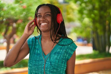 Parkta müzik dinlerken kendinden emin gülümseyen Afrikalı Amerikalı kadın.