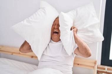 Yaşlı gri saçlı adam yatak odasındaki gürültü için kulaklarını kapatıyor.