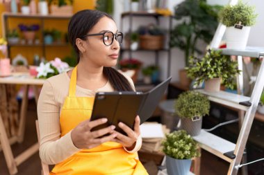 Young arab woman florist using touchpad sitting on chair at flower shop