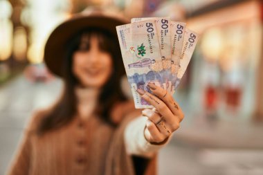 Kışlık şapkalı esmer kadın gülümsüyor elinde Kolombiya pezosu gün batımında şehirde paralar tutuyor.