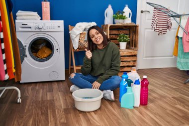 Young hispanic woman doing laundry washing by hand smiling happy and positive, thumb up doing excellent and approval sign 