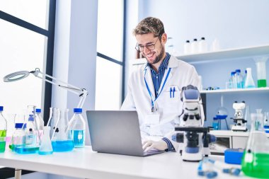 Young man scientist smiling confident using laptop at laboratory
