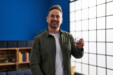 Genç beyaz adam evde dikilip bir bardak viski içiyor.