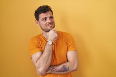 Sarı arka planda dikilen genç İspanyol bir adam bir soru hakkında endişeli ve gergin bir şekilde düşünüyor. 