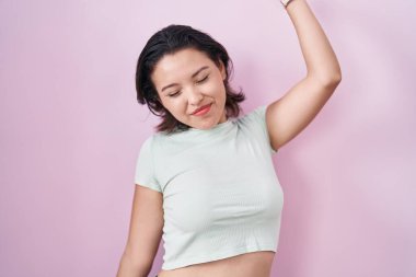 Hispanic young woman standing over pink background stretching back, tired and relaxed, sleepy and yawning for early morning 