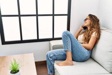 Evdeki kanepede oturmuş akıllı telefondan konuşan genç, güzel İspanyol kadın.