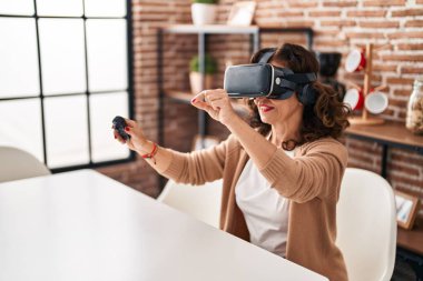 Orta yaşlı İspanyol kadın evde sanal gerçeklik gözlüğü takıyor.