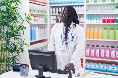 Eczanede bilgisayar kullanarak gülümseyen Afrikalı Amerikalı kadın eczacı.