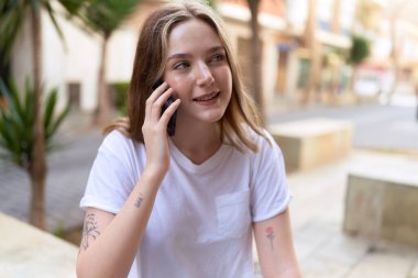 Beyaz bir kadın gülümsüyor ve caddede akıllı telefondan konuşuyor.