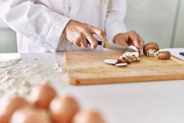 Young woman wearing cook uniform cutting mushrooms at kitchen