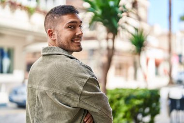 Genç İspanyol adam gülümsüyor. Kendine güveni tam. Sokakta çapraz hareketlerle duruyor.