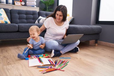 Anne ve oğlu dizüstü bilgisayar kullanıyor ve evde yerde oturuyor.