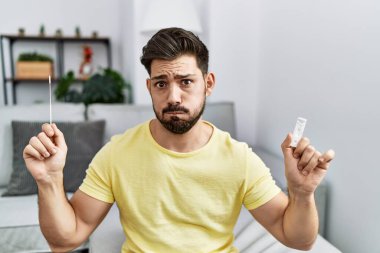 Young man with beard holding coronavirus infection nasal test puffing cheeks with funny face. mouth inflated with air, catching air. 