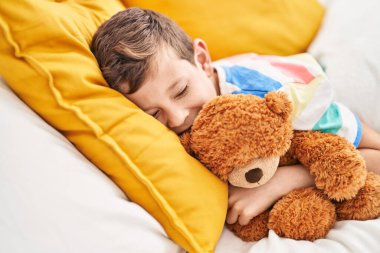 Sarışın çocuk oyuncak ayıyı kucaklıyor yatak odasında uyuyor.