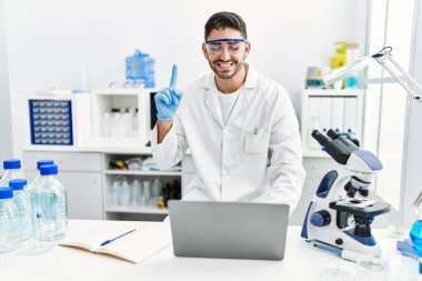 Laboratuvarda çalışan genç İspanyol bir adam dizüstü bilgisayarla gülümsüyor bir fikirle ya da soru işareti yaparak mutlu bir yüzle, bir numara 