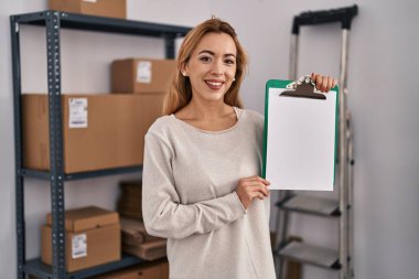 Küçük bir iş yerinde çalışan İspanyol kadın elinde boş alanı olan bir pano tutuyor. Olumlu ve mutlu görünüyor. Kendine güvenen bir gülümsemeyle dişlerini gösteriyor. 