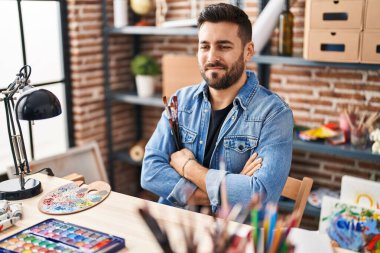 Masada oturan İspanyol genç adam sanat stüdyosunda kollarını kavuşturdu.