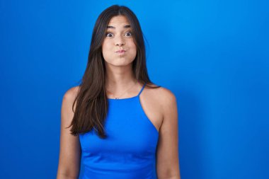 Mavi arka planda dikilen İspanyol kadın komik yüzlü yanakları şişiriyor. Havayla şişmiş ağız, çılgın bir ifade.. 