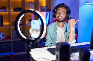 Dövmeleri olan genç İspanyol bir adam akıllı telefonuyla özel ders kaydediyor. Parmağını yana doğru uzatıyor ve ağzı açık gülümsüyor. 