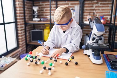 Sınıfta not defterine yazı yazan sevimli bir çocuk.